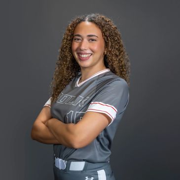 Smiling female softball player in uniform crossing arms.