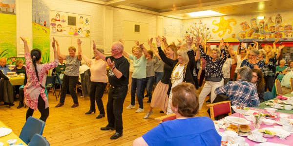 a group of people of different ages, genders and ethnicities copy dance moves from a Bollywood tutor