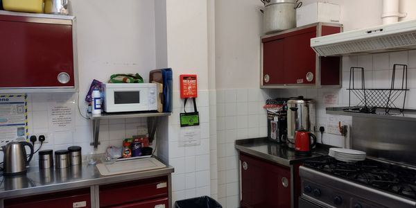 an image of a kitchen showing a microwave, stove, kettle and cabinets. a fire blanket is on the wall