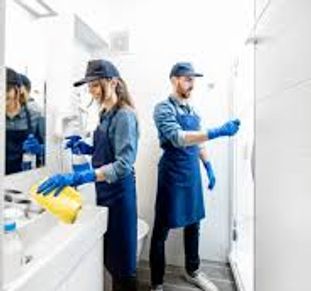 Two professional cleaners cleaning a bright bathroom with gloves and aprons.
