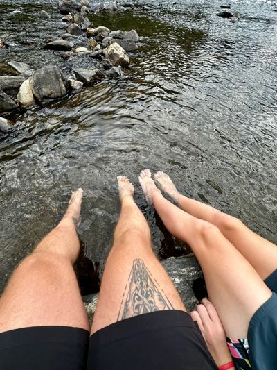 Two people soaking their feet in a river near rocky banks.
