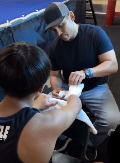 Man wrapping another man's hand with boxing tape.
