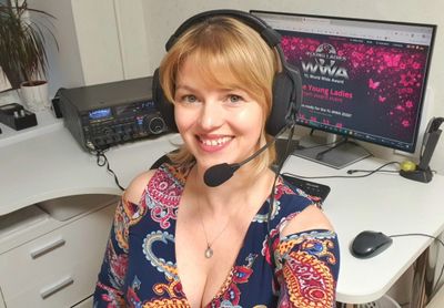 Smiling woman wearing a headset in front of a computer screen showing an award event.