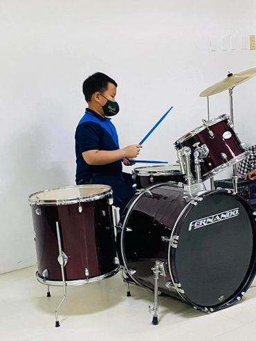 Young boy playing a Fernando drum set wearing a face mask.