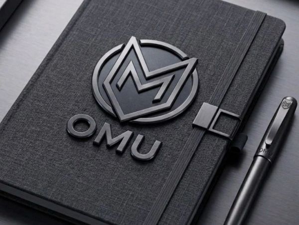 Black OMU notebook with matching pen on a dark surface.