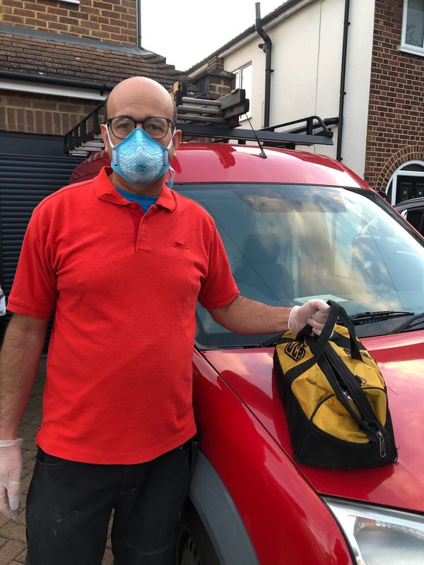 Man in a red shirt with a mask and gloves holding a yellow bag by a red car.