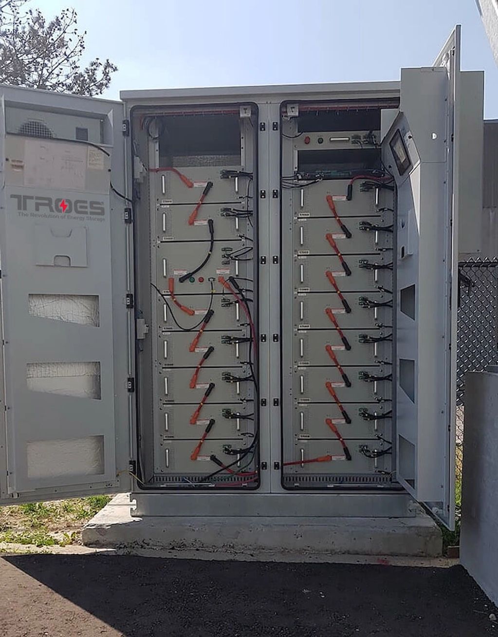 Enclosure on concrete pad with doors open, showing lithium ion battery bank connected with cables.