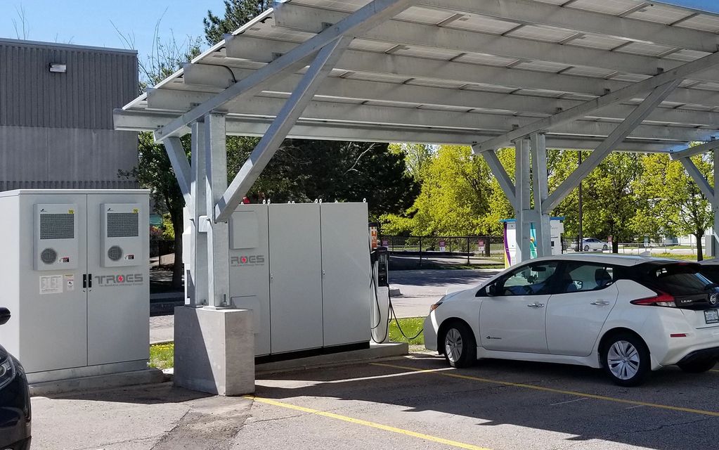 solar array on posts above electric vehicle plugged into EV Charger. Battery pack is nearby.