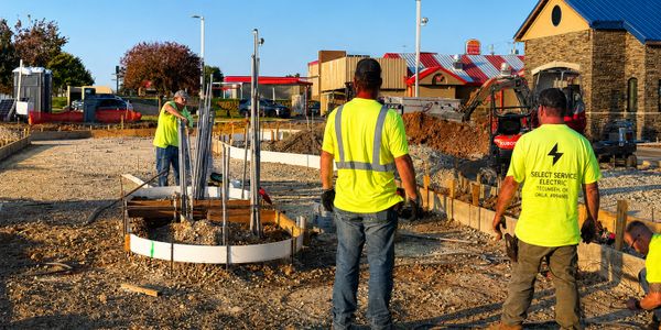 Construction workers in bright yellow shirts working on a foundation site.