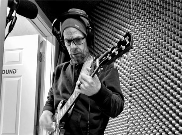 Man wearing headphones and a beanie playing electric guitar in soundproof room.