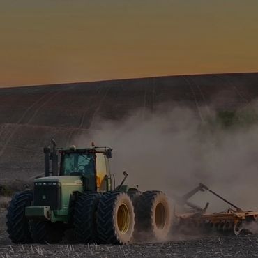 A tractor plowing a dusty field at sunset.