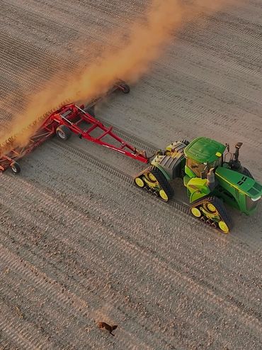 Green tractor tilling soil in a field, creating dust clouds.