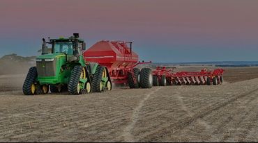 A green tractor with tracks pulling red farming equipment across a field at dusk.