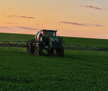 Farm tractor spraying crops in a green field at sunset.