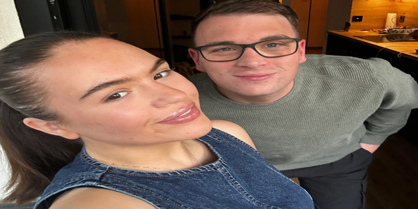 Two people smiling indoors for a close-up selfie.