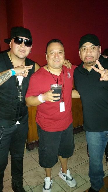 Three men posing together indoors, two making peace signs.
