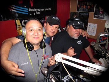Three men posing with headphones and DJ equipment in a radio studio.