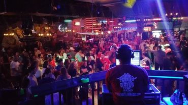 DJ playing music to a lively crowded bar dance floor.