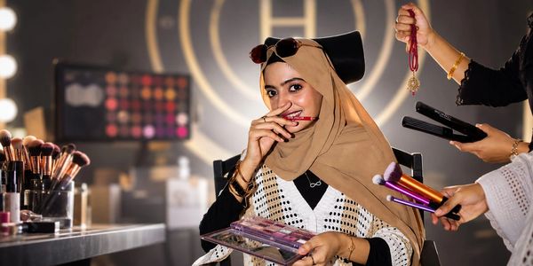 Woman in a hijab applying makeup with brushes and palette.