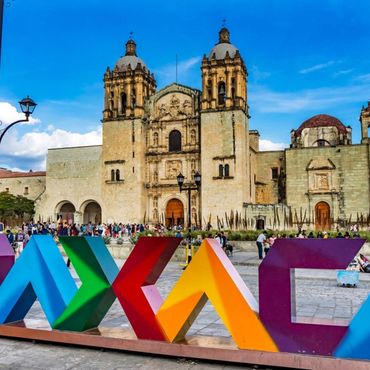 Colorful Oaxaca sign in front of a historic church with blue sky.