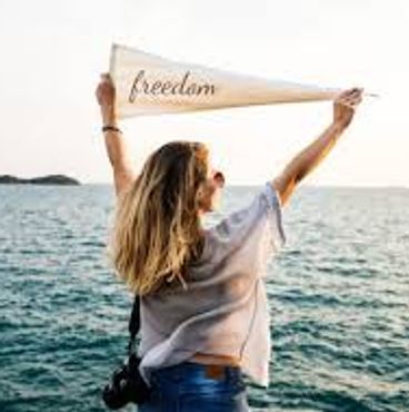 Woman by the sea holding a 'freedom' flag.