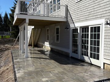 Newly constructed patio with stamped concrete under a raised deck beside a house.
