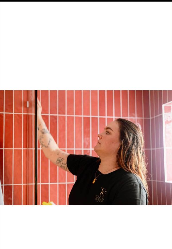 Woman cleaning glass in red-tiled bathroom.