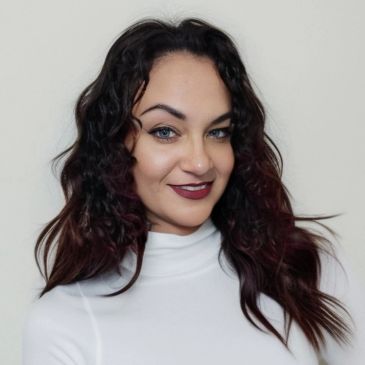 Woman with dark curly hair and white top smiles.