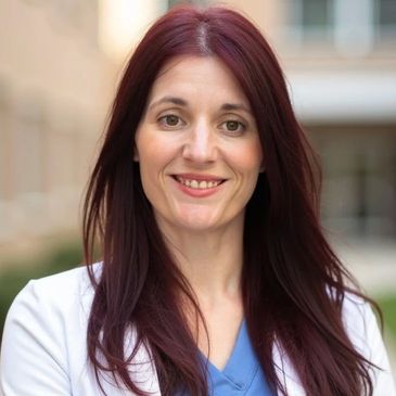 Smiling woman with long red hair in a white coat.