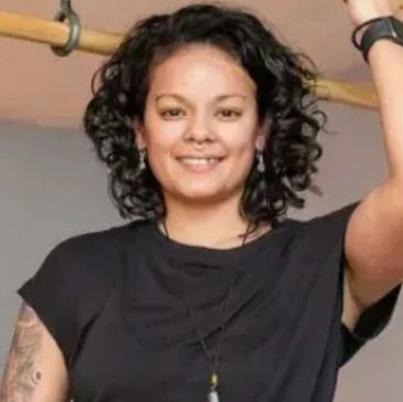 Smiling woman with curly hair and tattoos.