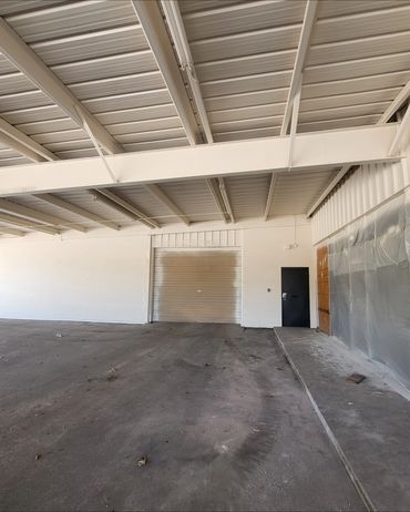 Empty industrial warehouse space with a closed garage door and a black pedestrian door.