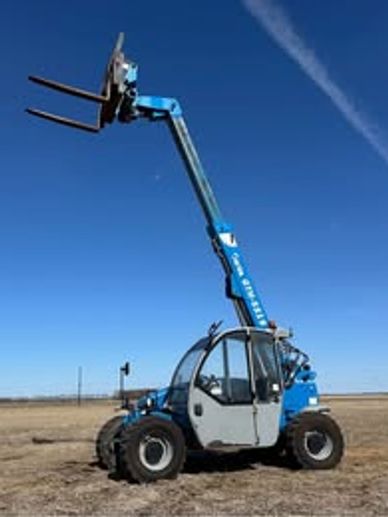 Blue telescopic forklift on dry ground under a clear sky.