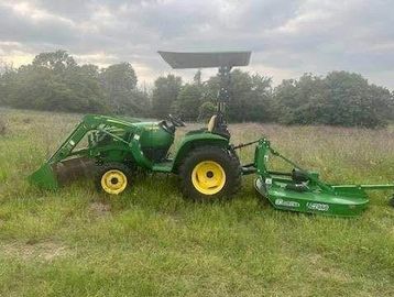 Green tractor with a mower attachment in a field.