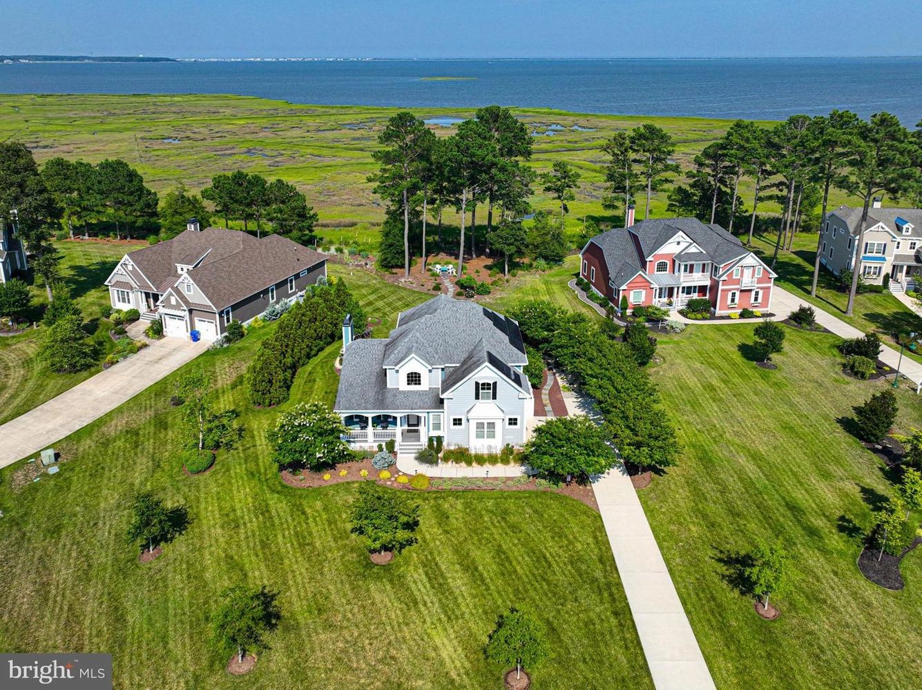 A charming gray house on a grassy hill by the ocean under a clear blue sky.