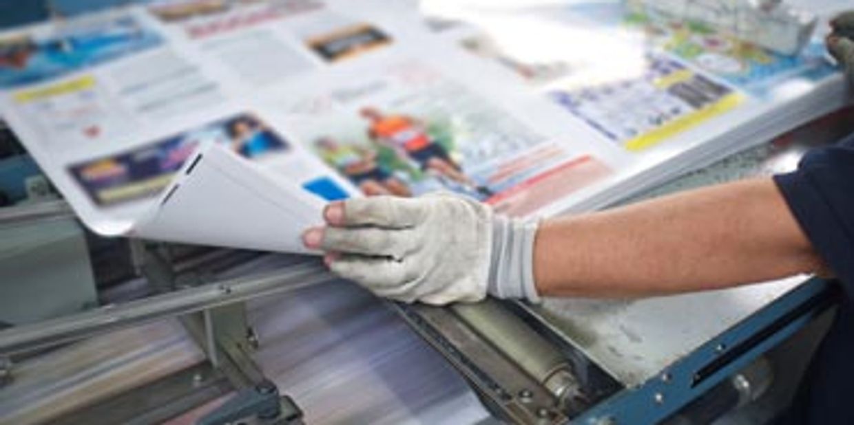 Closeup of an offset printing press operator viewing a press sheet for quality control.
