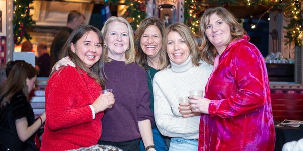 Five women smiling and posing together at a festive gathering.