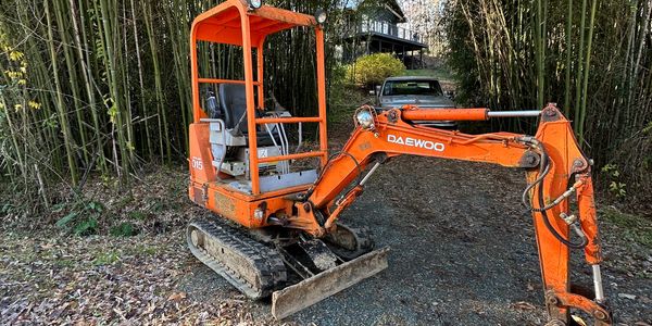 Orange Daewoo mini excavator outdoors on dirt path.