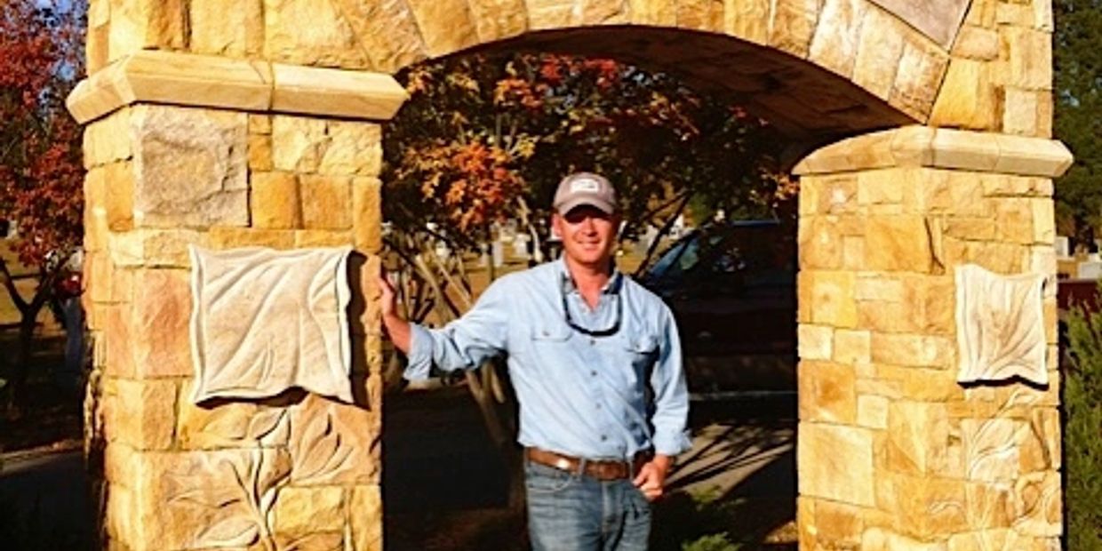 Man standing under a stone archway outdoors.