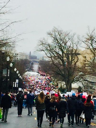 Crowd of people marching on a city street with signs and umbrellas.