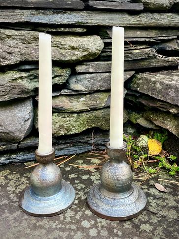 Two tall white candles in rustic metal holders on a stone surface.