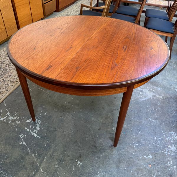 Round wooden dining table with tapered legs in a mid-century style.