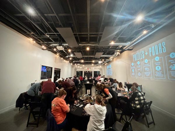 People solving puzzles together in a well-lit room with instructions projected on the wall.