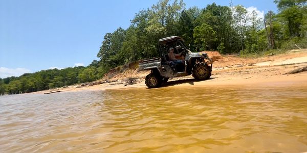 An off-road vehicle with a rider parked on a sandy lakeshore under a clear sky.