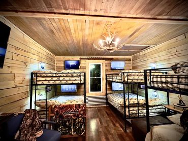 Rustic bunkhouse room with four bunk beds and mounted TVs.