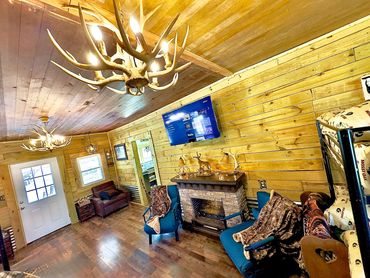 Cozy wooden cabin living room with antler chandeliers and a stone fireplace.