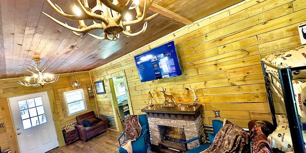 Cozy wooden cabin living room with antler chandeliers and a stone fireplace.