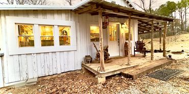 Cozy rustic white cabin with warm interior lighting and a wooden porch.