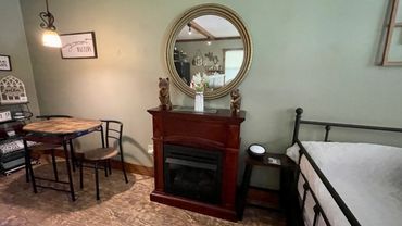 Cozy room with a round mirror, small fireplace, dining table, and metal bed frame.