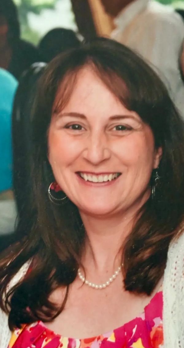 Smiling woman with dark hair wearing pearl necklace and colorful dress.