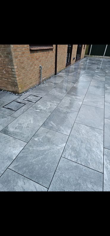 Newly installed wet grey stone patio tiles beside a brick house.